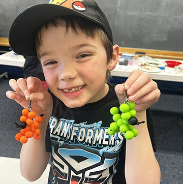 Happy student in the Birch Buddies program holding up orange and green beads