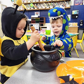 Two young students dressed as a bee and dinosaur stirring a black pot