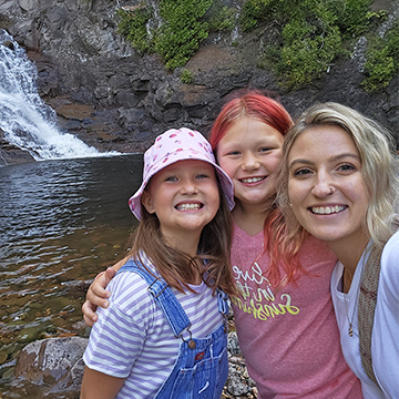 Teacher and two students smiling for a picture in front of a waterfall