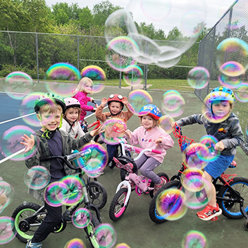 Summer Saplings students riding bikes around bubbles