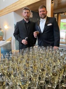 Two men standing by table of champagne glasses