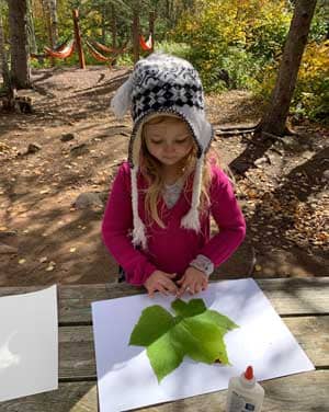 Girl putting a leaf on a piece of paper