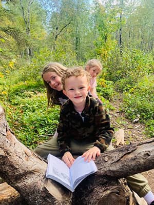 Three happy students outside in the forest with a book