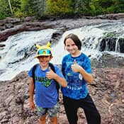 Two students by a waterfall with their thumbs held up