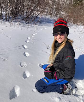 Girl outside in the snow next to animal tracks