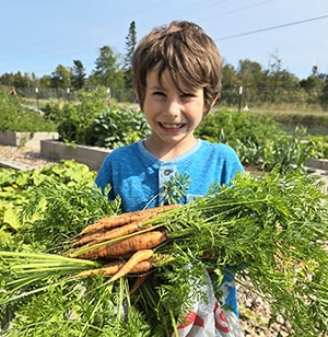 Happy student outside holding up freshly picked carrots