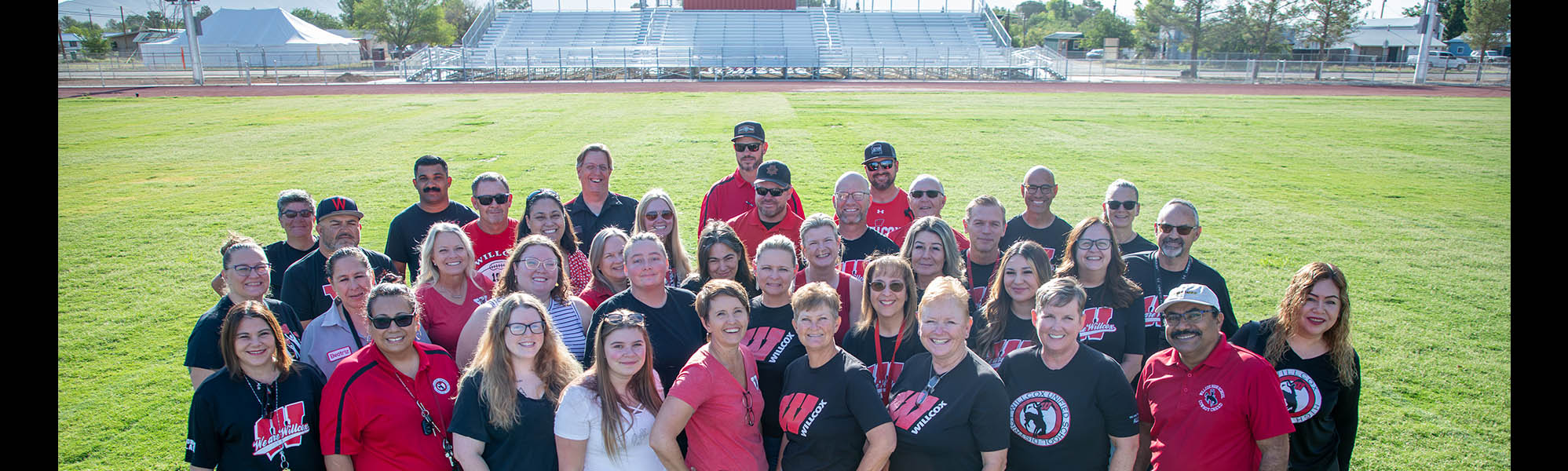 Happy staff members wearing red and black posing for a group photo on the football field