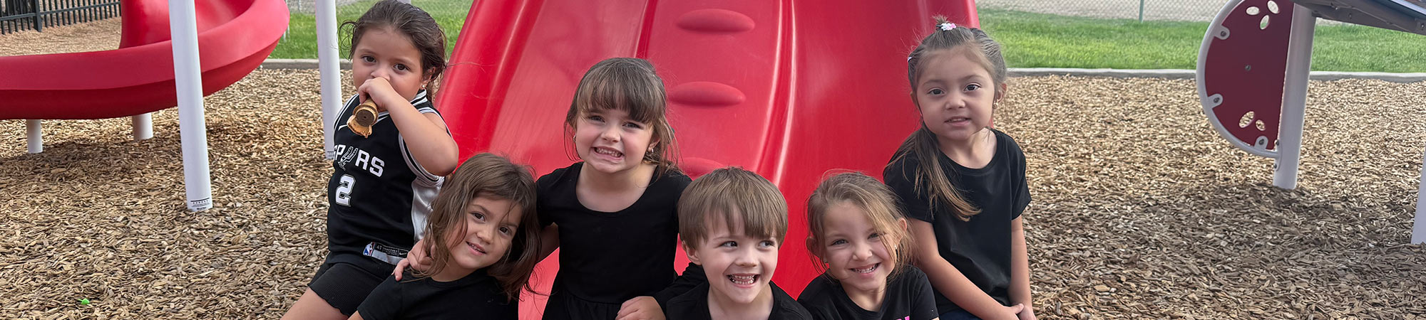 Preschool kids sitting on the playground together and smiling