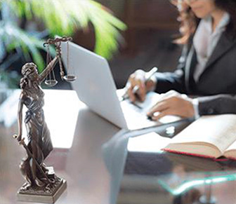 Woman working on a laptop and a small Lady Justice statue on the desk.