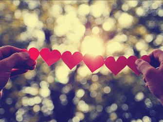 An adult holding up a string of paper hearts up to the evening sky