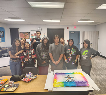Students standing behind a colorful cake