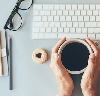 Parent holding cup of coffee next to keyboard