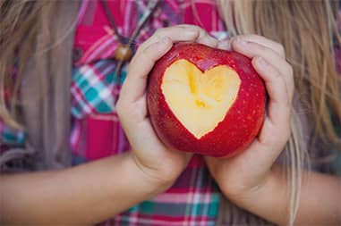 Schoolgirl holding up a red apple with a heart-shaped bite