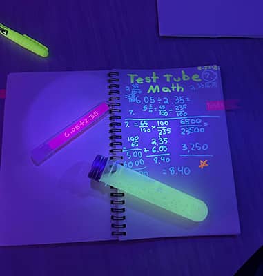 Notebook under a blacklight that says Test Tube Math with glowing math problems