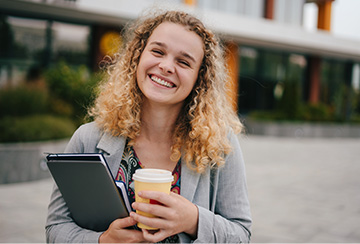 Woman with coffee smiling outside campus