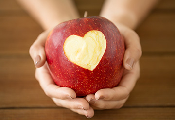 Woman holding a red apple with a heart-shaped bite