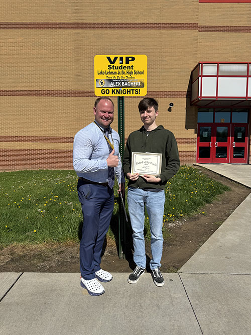 Principal giving thumbs up in photo with student of the month outside