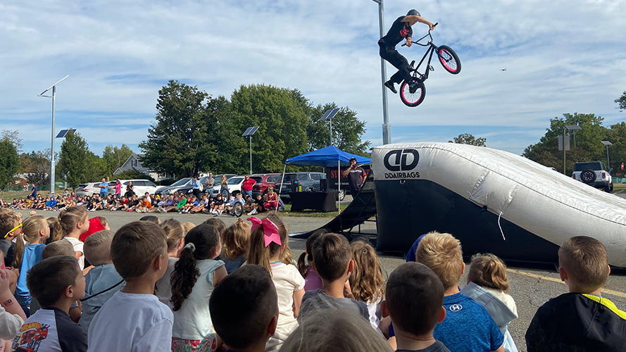 Students outside watching someone on a bike making a jump