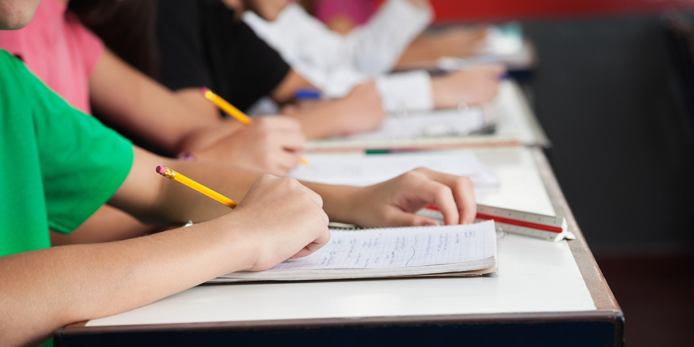 Students hands holding pencils to write in notebooks