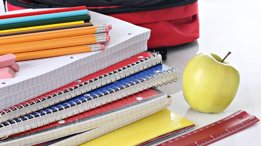 Colorful school supplies next to a backpack and apple