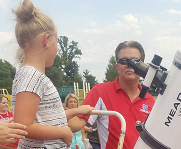 Adults helping a student look through a telescope