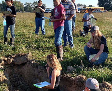 Students working in a field with a hole in the ground