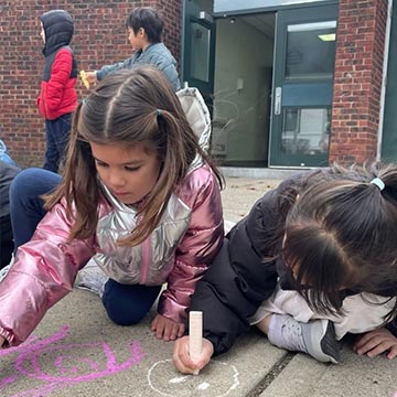 Students drawing with chalk on the floor in front of the school entrance