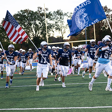 Football players running onto the field holding flags