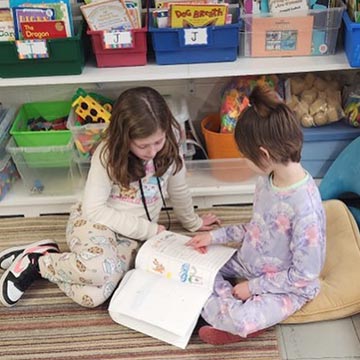 Two students reading a book on the floor Two students reading a book on the floor