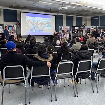 Parents sitting on the bleachers and smiling Parents attending Curriculum Preview Night