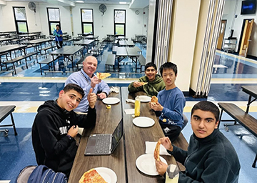 Group of students eating pizza with principal