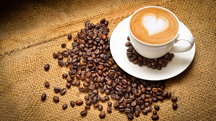 Coffee beans and a coffee cup filled with coffee with a white heart in it
