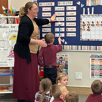 Teacher standing next to a student who is pointing out the month name