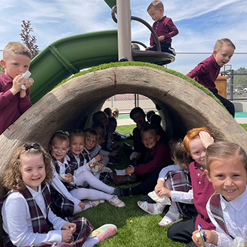 Students sitting on and under a playground tunnel