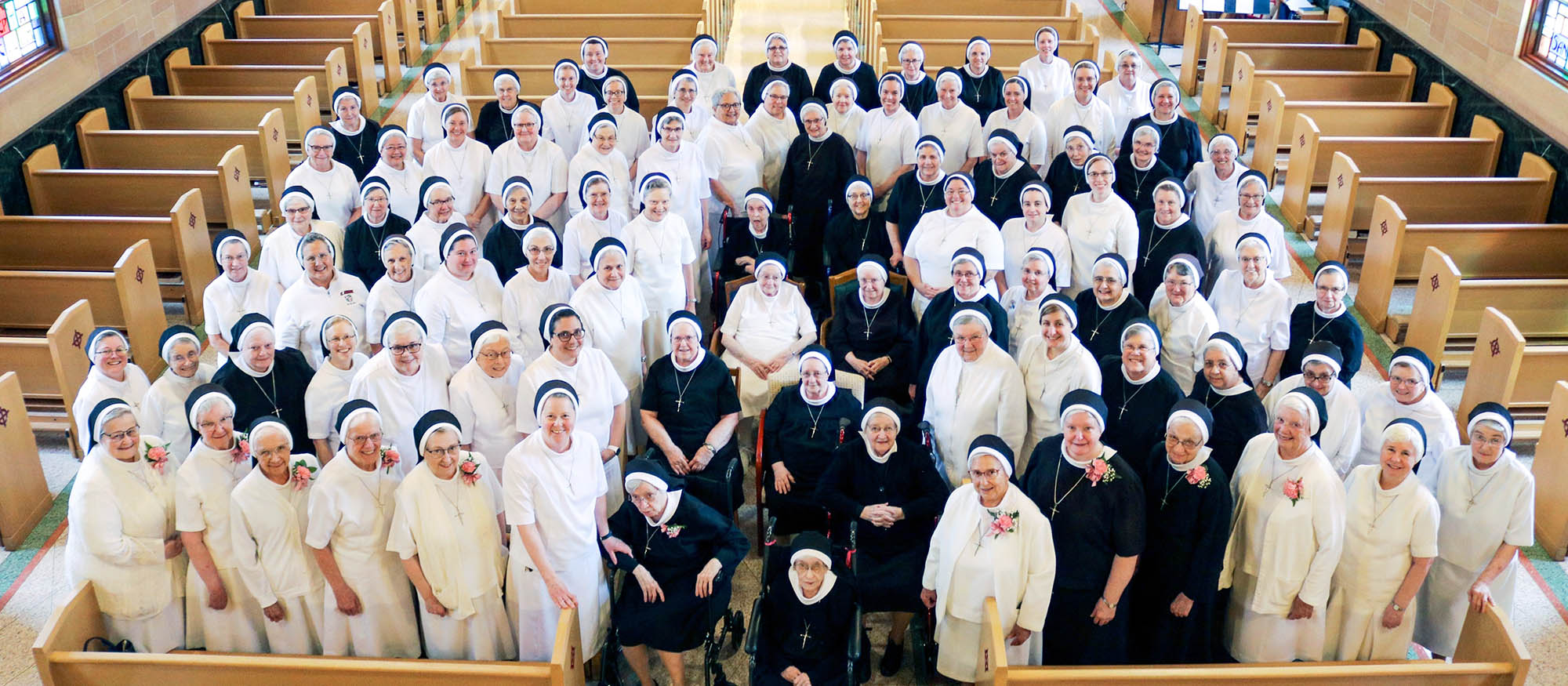 Aerial view of Province group Sisters smiling for the camera from pews in a beautiful church