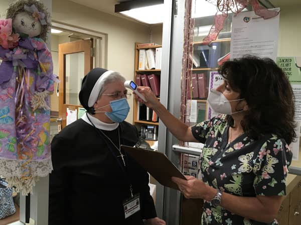 sister in mask getting temperature taken on her forehead