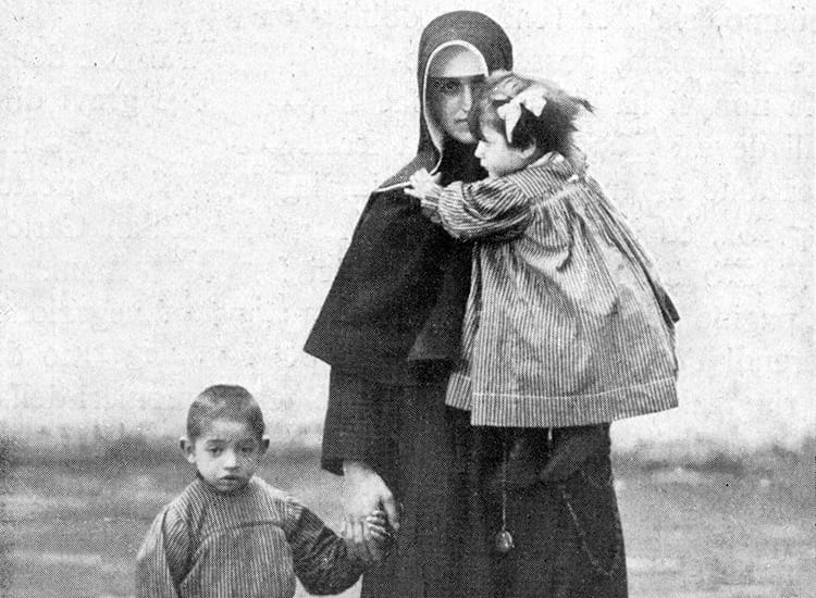 Sister holding one child in her arms and holding another's hand