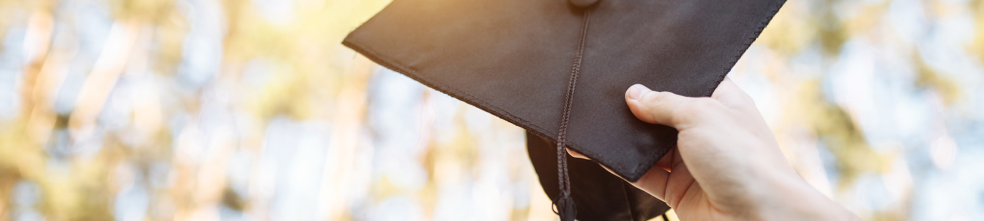Graduate holding up graduation cap toward the sky