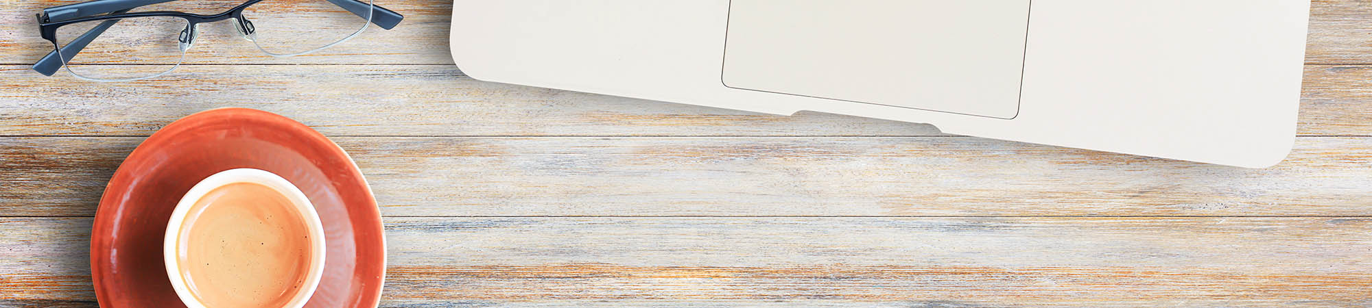 Cup of coffee, glasses, and laptop on a desktop