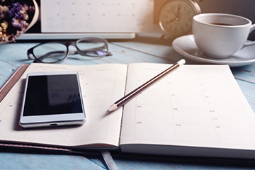 Desk with phone, planner, pencil, glasses, and cup of coffee