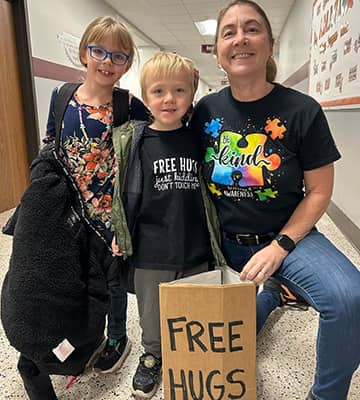 Two kids and an adult behind a sign that reads Free Hugs