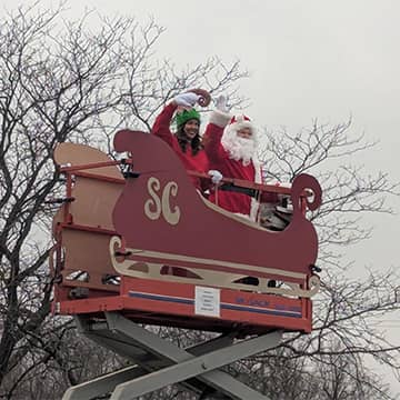 Santa and an adult waving in a sleigh on a lift
