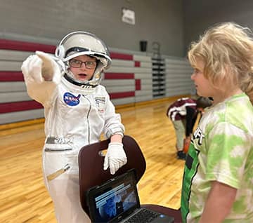 Student in a NASA outfit pointing the way for another student
