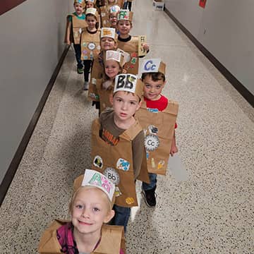 Students walking down the hall with cutout bags over their shirts and paper hats representing letters of the alphabet