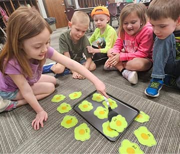 Students watching another student move eggs on a cookie sheet