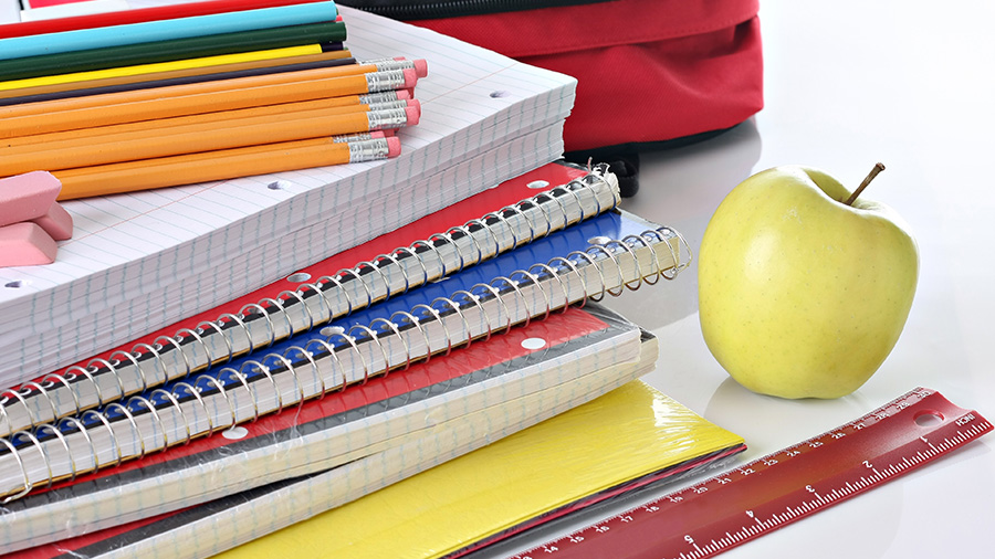 Colorful school supplies next to a golden apple