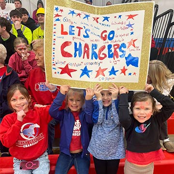 Students holding up a sign that says Lets Go Chargers!