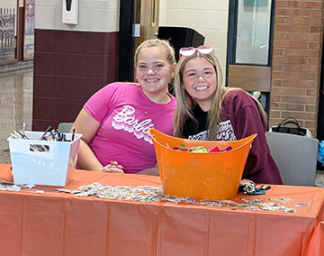 Two happy students helping behind an information table