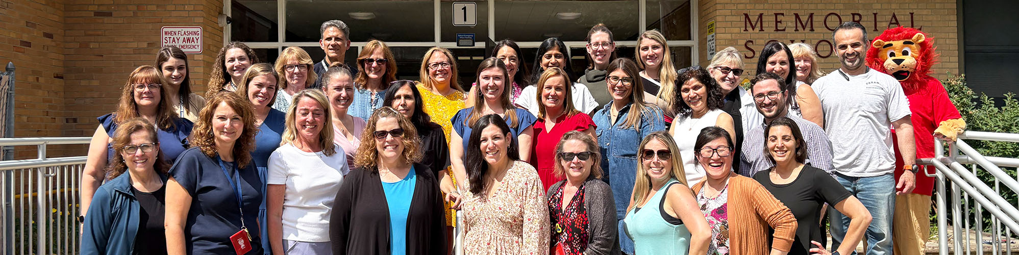 Happy staff members on the school stairs with principal and school mascot