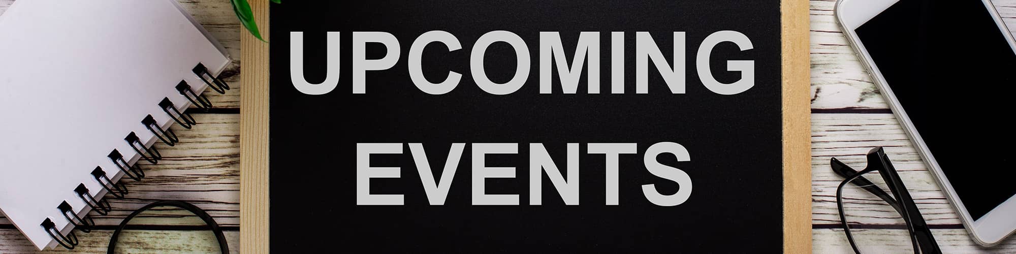 Phone, eyeglasses, and a notebook next to a sign that reads Upcoming Events